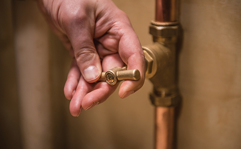 Hand turning a stop tap under the sink