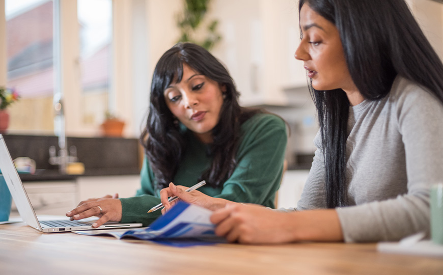 Two customers sat at a table looking at a laptop and bills